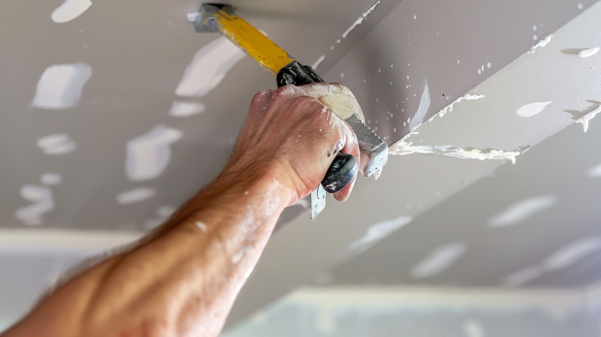 Close-up of a hand using a putty knife to smooth drywall compound on a ceiling