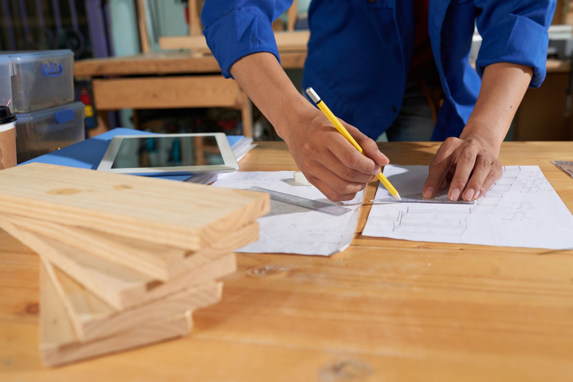 Person drawing plans on a workbench with wooden planks