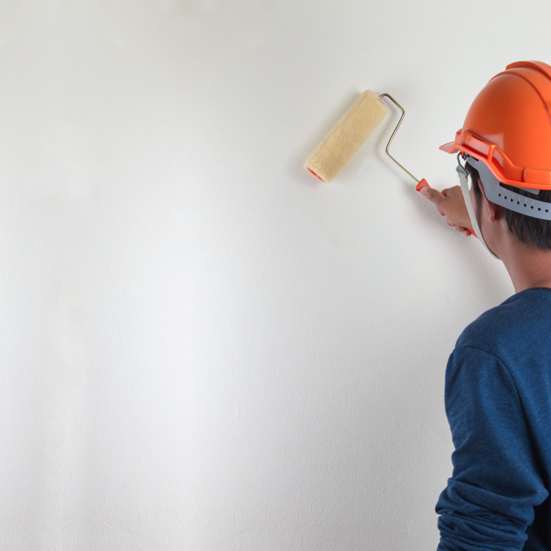Worker in an orange hard hat painting a wall with a roller brush