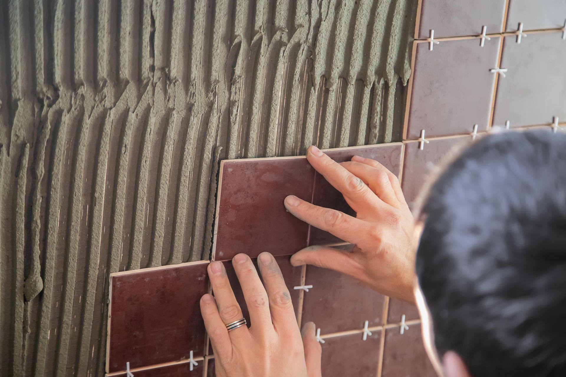 A person is laying tiles on a wall.