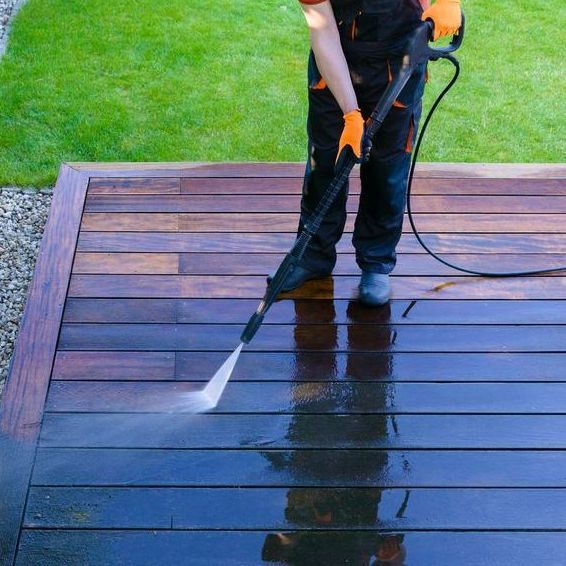 A man is using a high pressure washer to clean a wooden deck