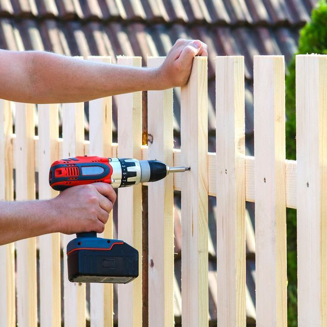 A person is using a drill to install a wooden fence.