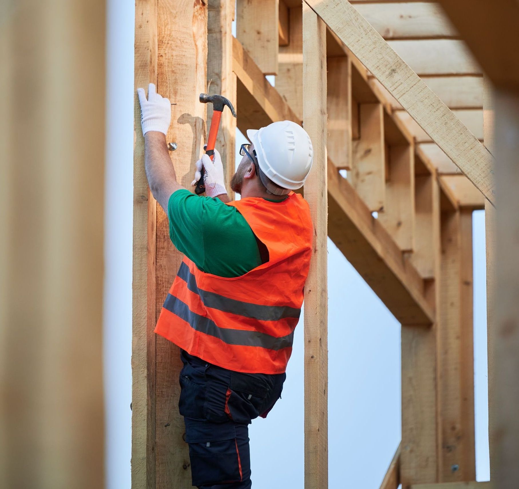 Construction worker in safety gear hammering nails into a wooden frame
