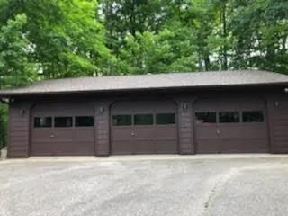 Three-car brown garage with black roof, set against a green wooded background.