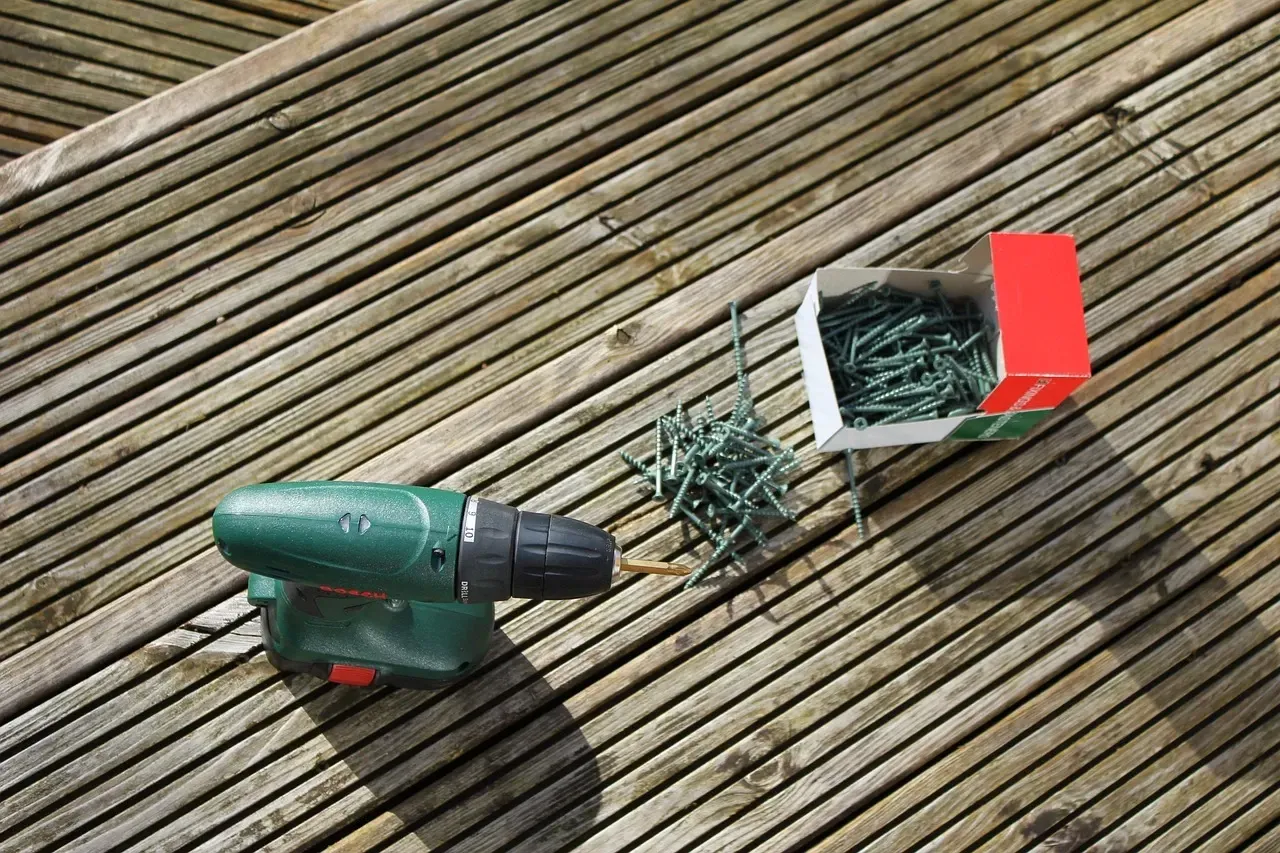 Green cordless drill next to a small white-and-red dustpan on a wooden deck