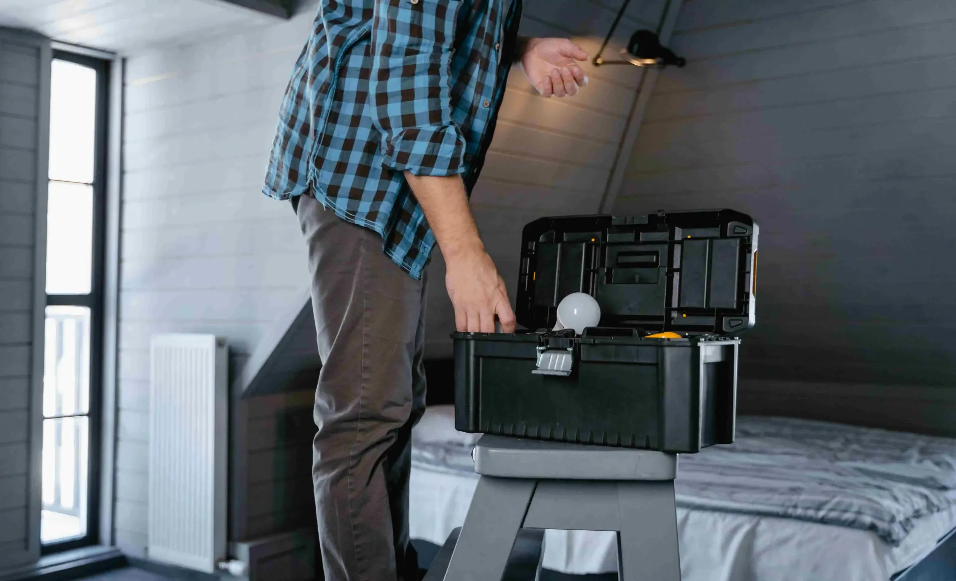 Person packing gear into a black case in a bedroom near a bed and window