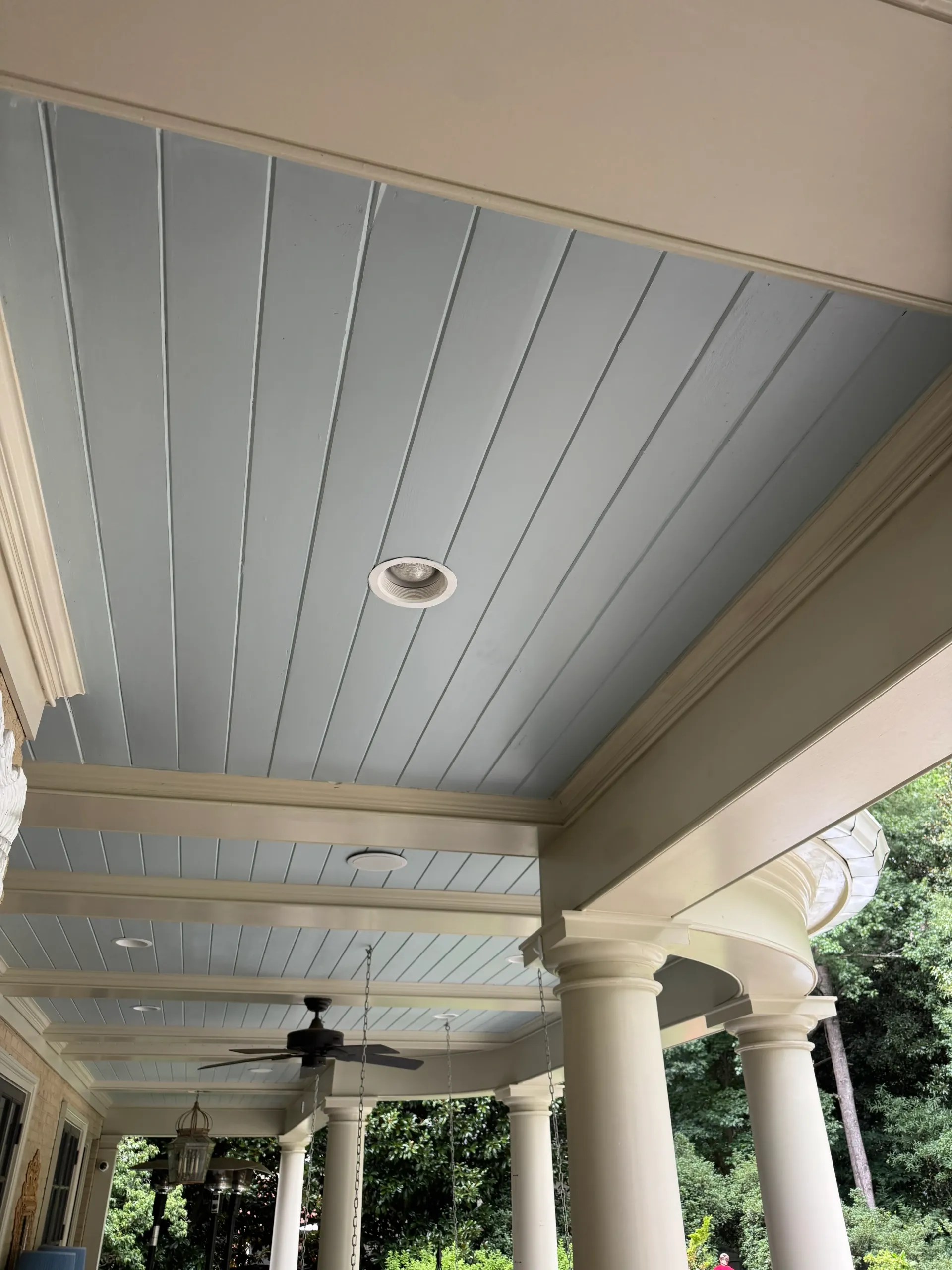 Covered porch ceiling with blue beadboard panels, white columns, ceiling fan, and recessed light.