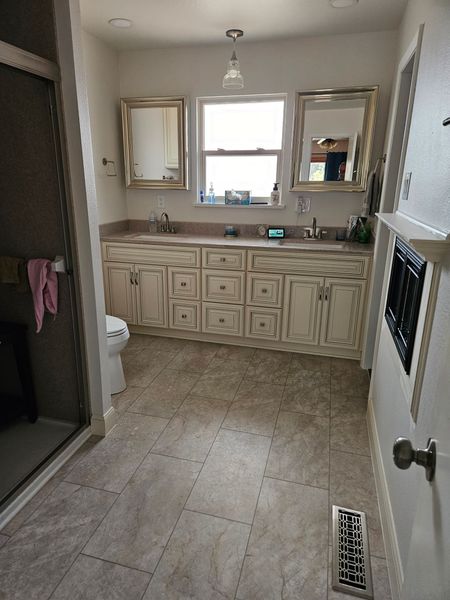 Bathroom with vanity, mirrors, shower on left, and tiled floor in a narrow room.