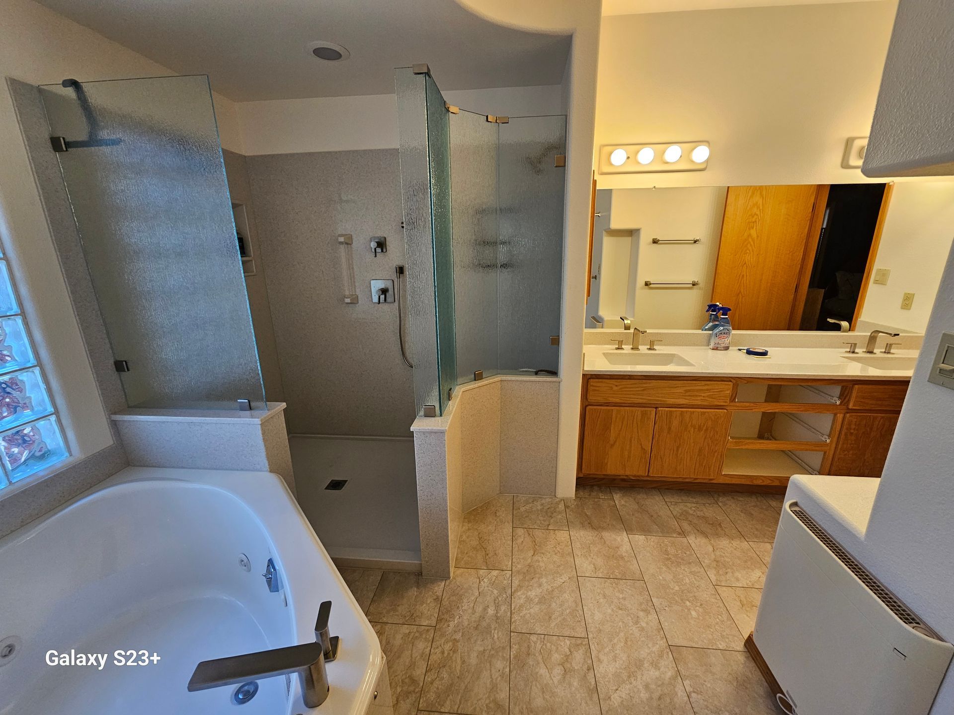 Bathroom with tub, glass shower, double vanity, wood cabinets, and tiled floor.