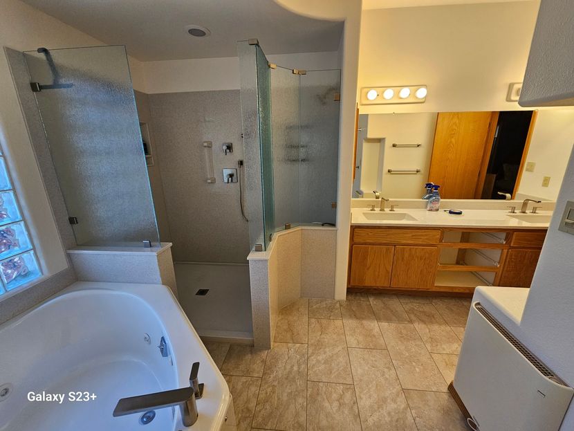 Bathroom with tub, glass shower, double vanity, wood cabinets, and tiled floor.
