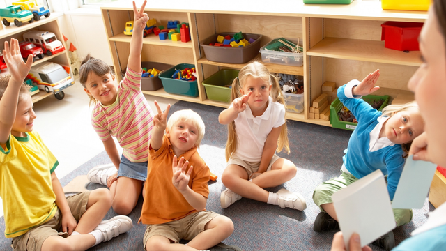 Smiling child in white shirt in a colorful classroom with other children playing in the background