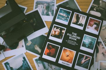 A black camera sitting on a wooden surface surrounded by numerous Polaroid-style photographs