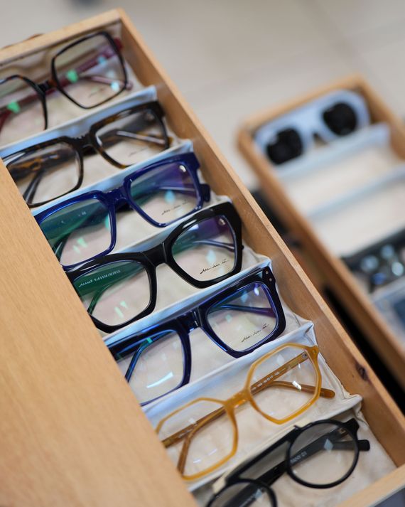 Occhiali esposti in un cassetto di legno. Le montature sono di vari colori e stili, tra cui nero, blu e marrone.