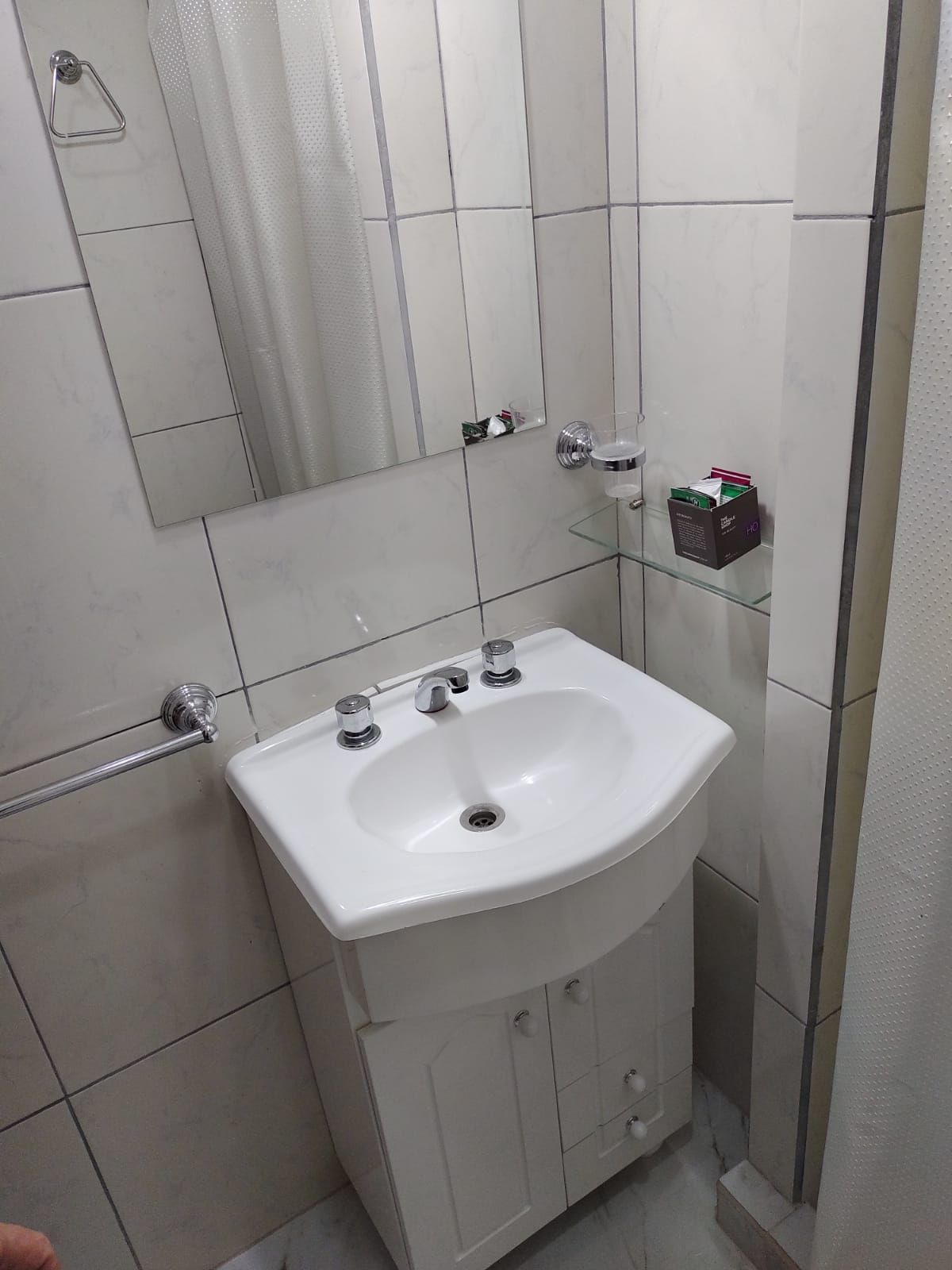 Pequeño baño con lavabo y mueble blanco, espejo y toallero en pared de azulejos.