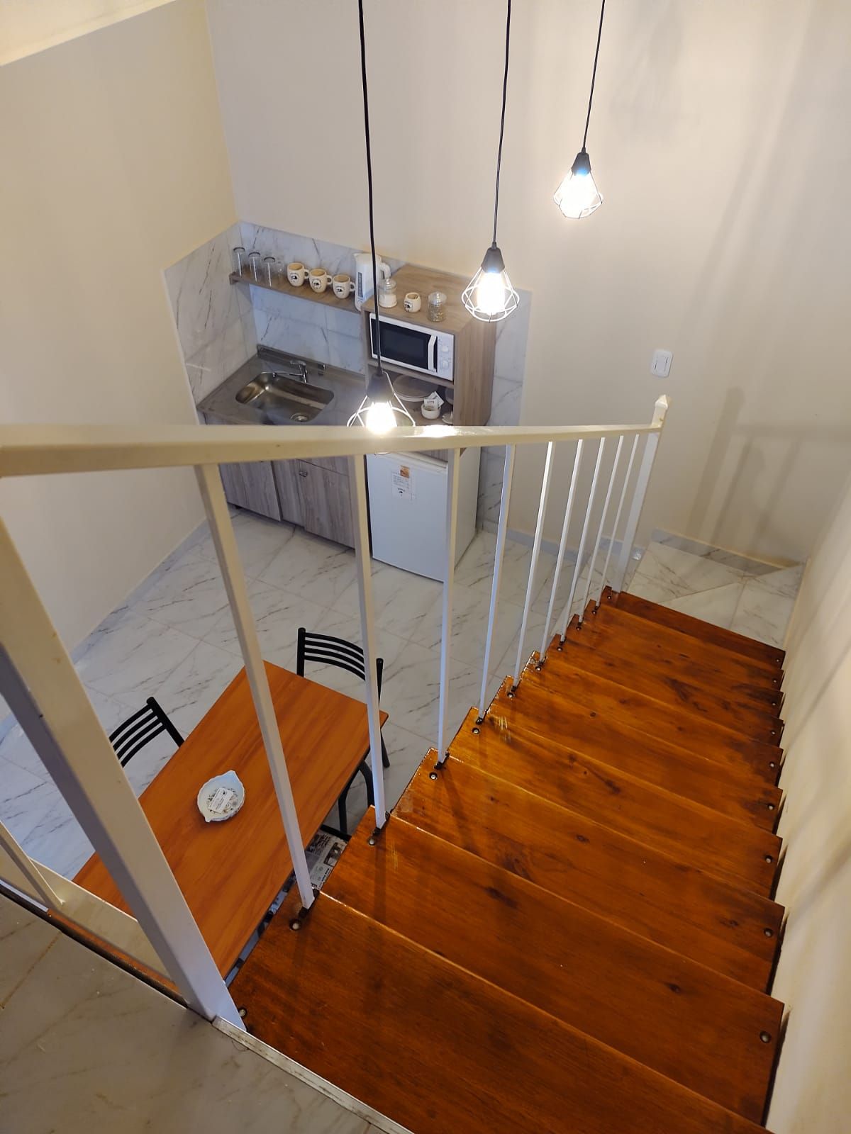 Unas escaleras de madera conducen a una zona de cocina-comedor con mesa, armarios y electrodomésticos.