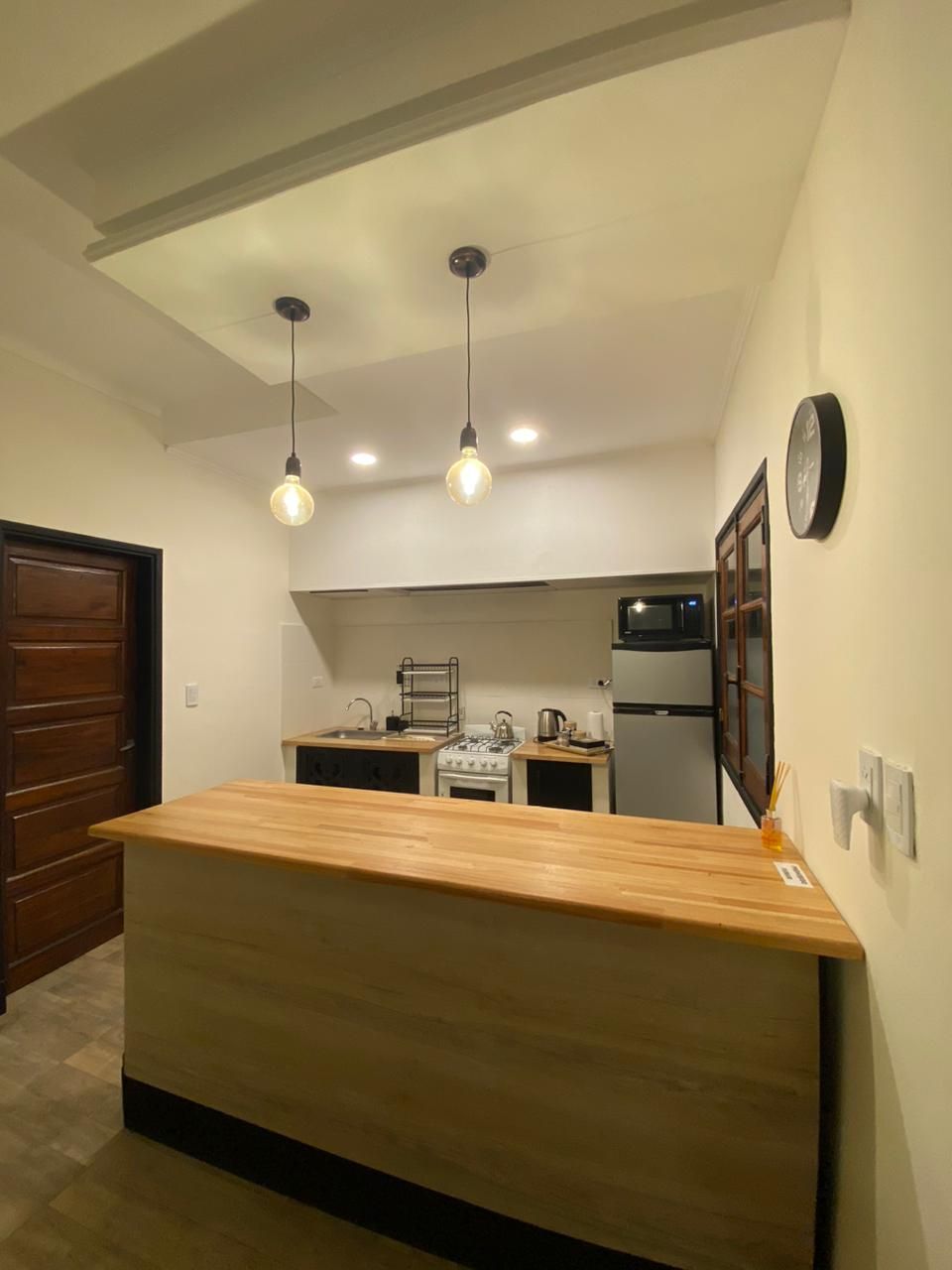 Pequeña cocina con encimera de madera, electrodomésticos de acero inoxidable y luces colgantes.