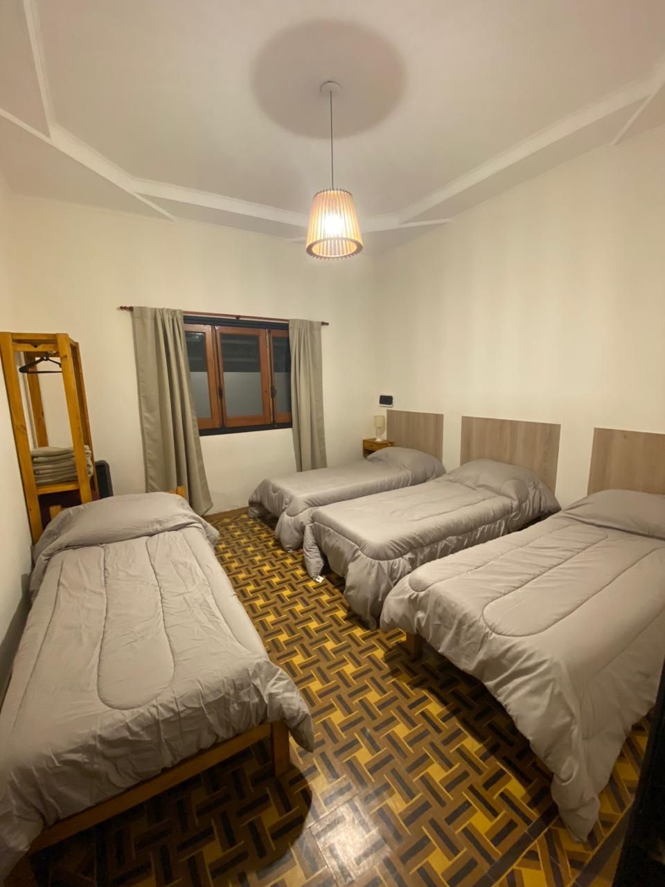 Cuatro camas individuales en una habitación con paredes de color canela, una ventana y piso de madera.