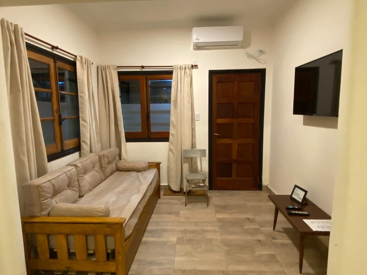 Acogedora sala de estar con muebles de madera, sofá, TV y puerta cerrada.