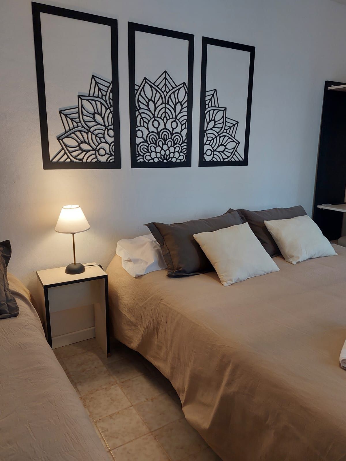 Dormitorio con cama, mesita de noche y decoración mural con mandalas. Combinación de colores beige y blanco.