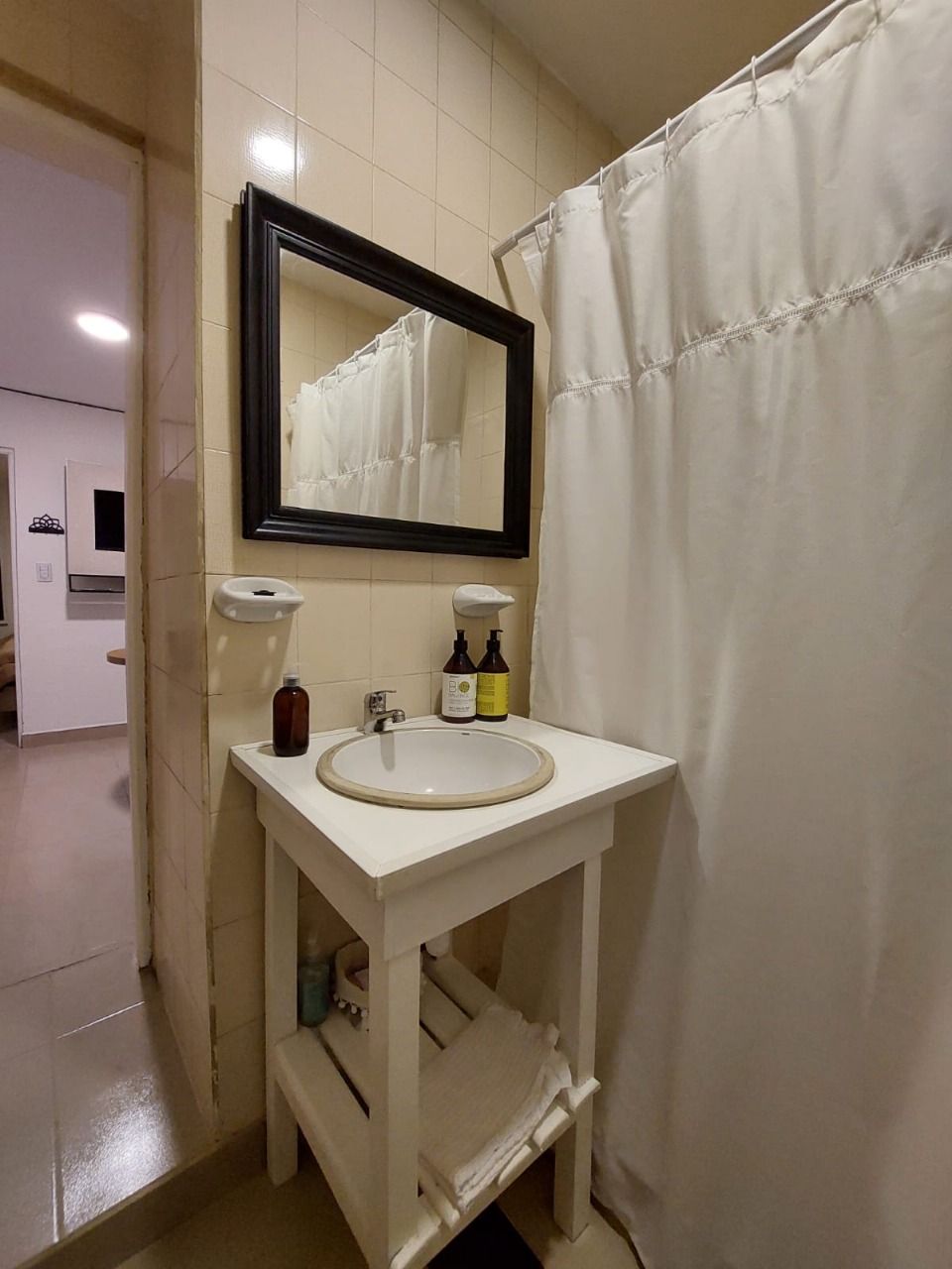 Tocador blanco con lavabo, espejo y cortina de ducha en un baño.