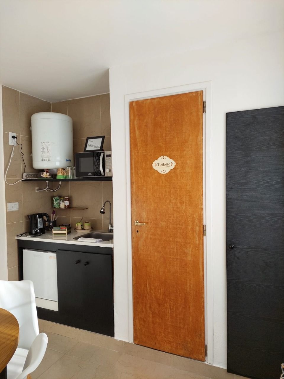 Pequeña área de cocina con paredes blancas, gabinetes negros y una puerta de madera marrón.