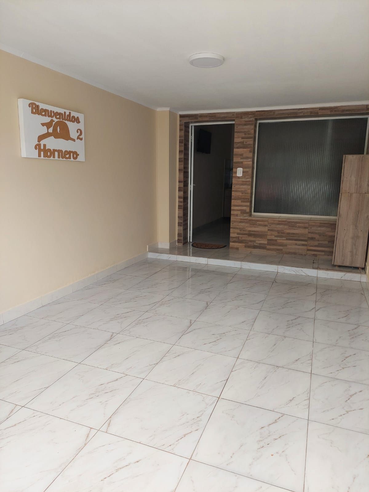 Habitación vacía con suelo de baldosas blancas, paredes color canela y una puerta. Un cartel en la pared dice 