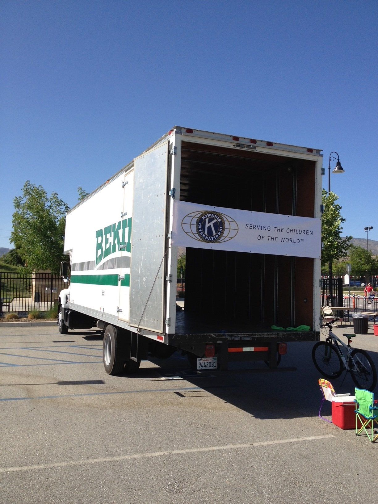 White box truck with open back in a parking lot. Banner on the inside shows a logo and text.