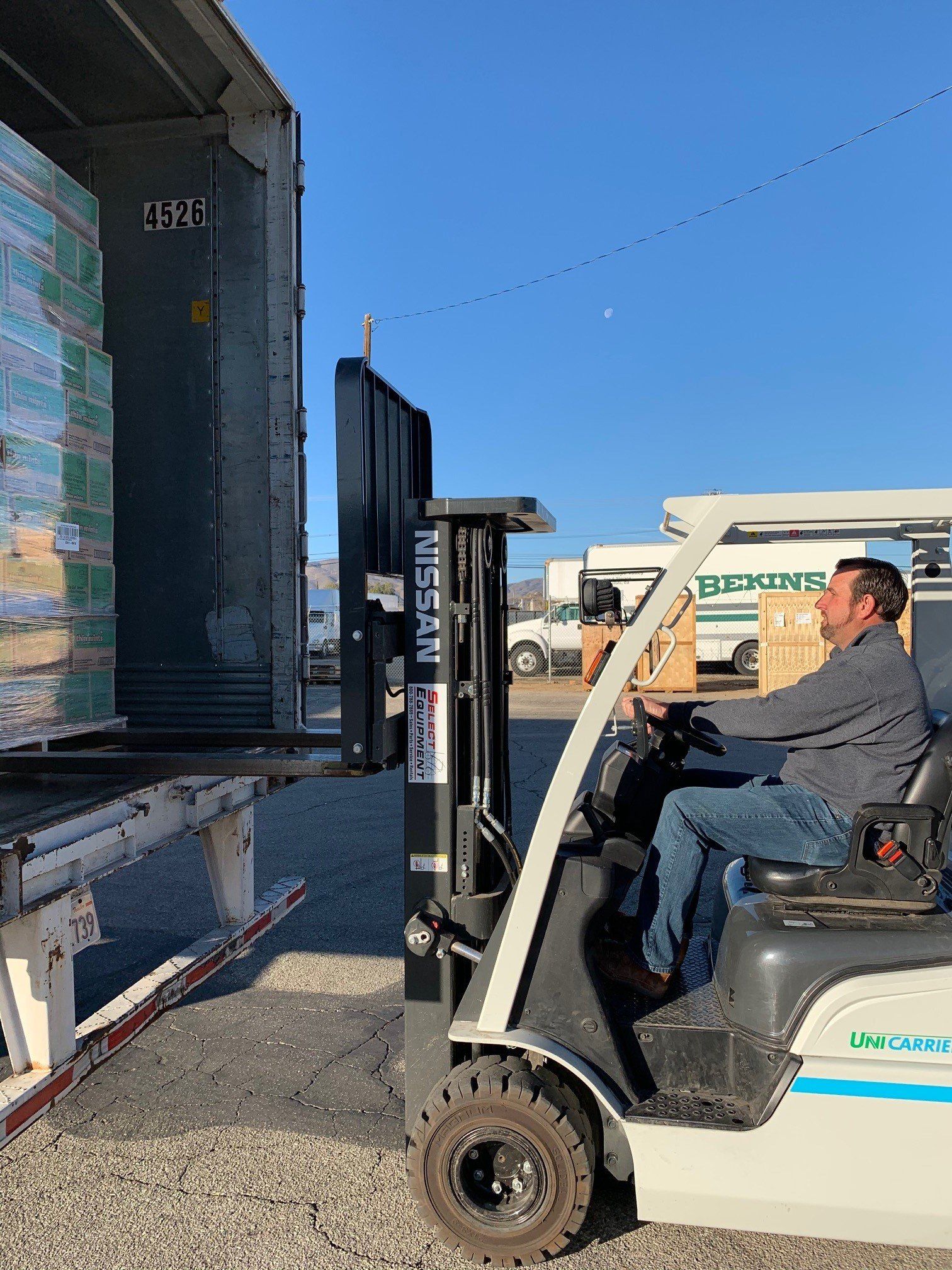 Forklift loading pallets from a semi-trailer on a sunny day. Man driving the forklift.