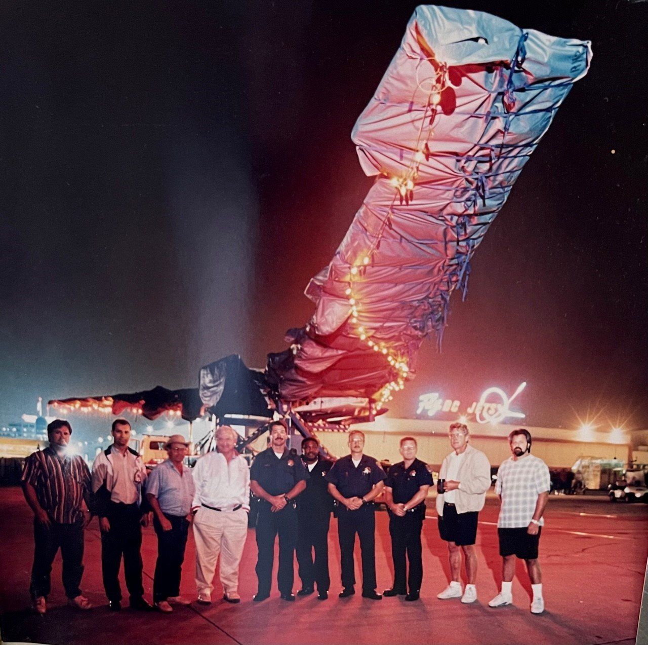 A damaged airplane, lit up at night, with a group of people standing in front of it.