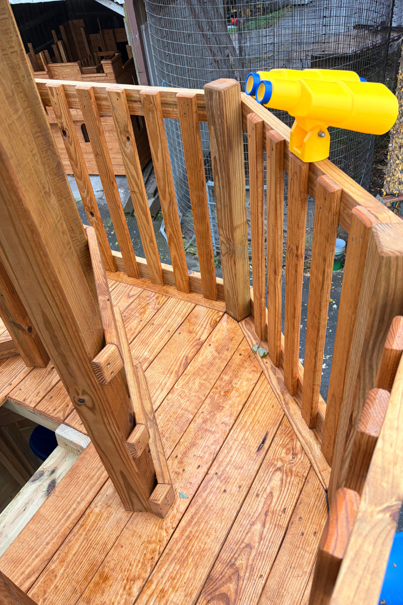 Upper wooden lookout deck of an Amish-built lighthouse playground featuring sturdy wooden railings, natural wood flooring, and bright yellow play binoculars for imaginative outdoor adventures.
 Copy
