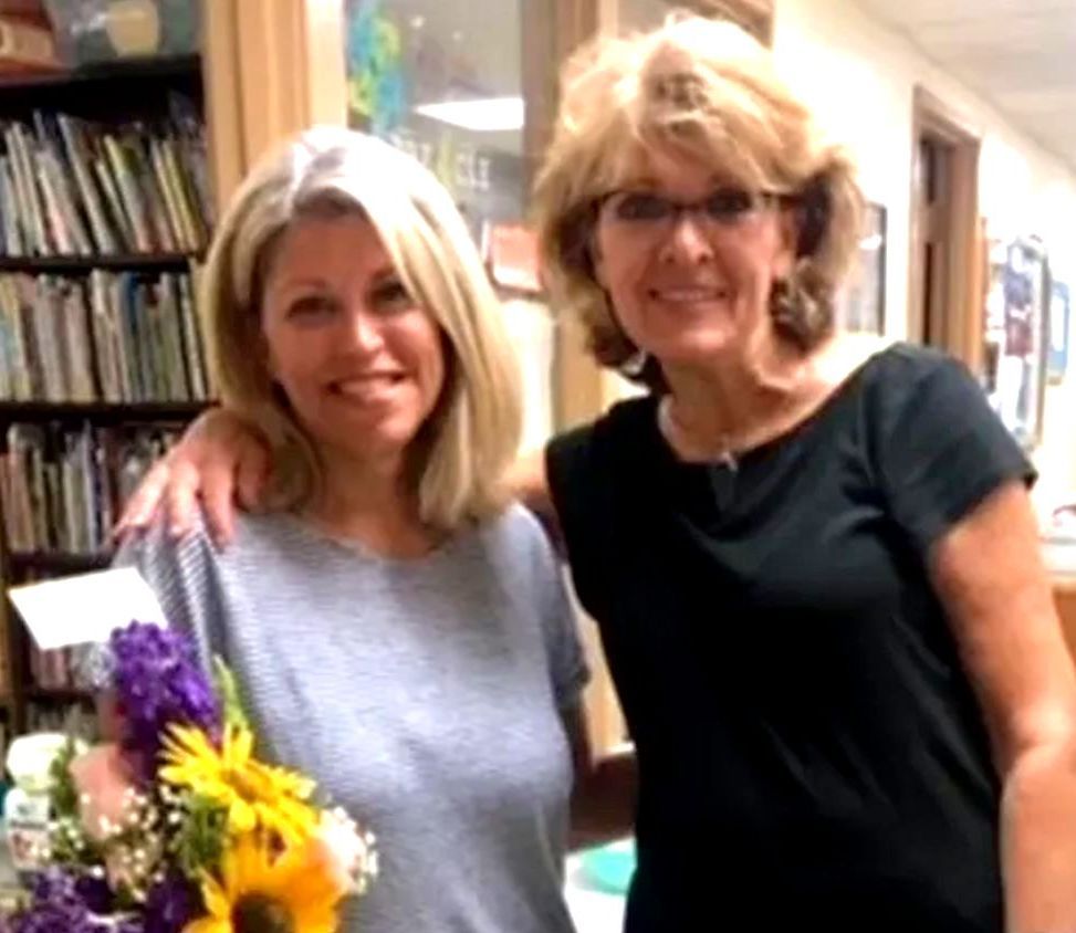 Two women posing for a picture with one holding a bouquet of flowers