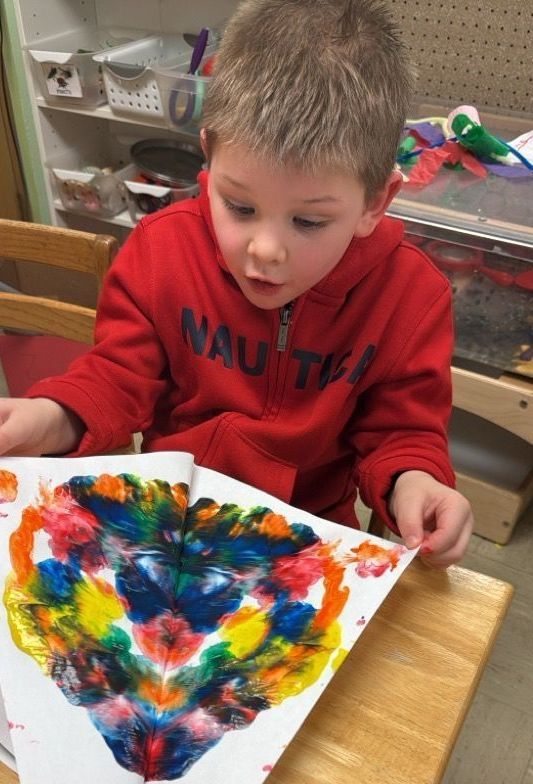 A young boy wearing a red nautica sweatshirt is painting a heart