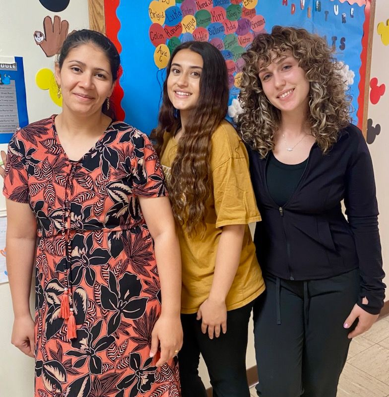 Three women are posing for a picture in front of a bulletin board