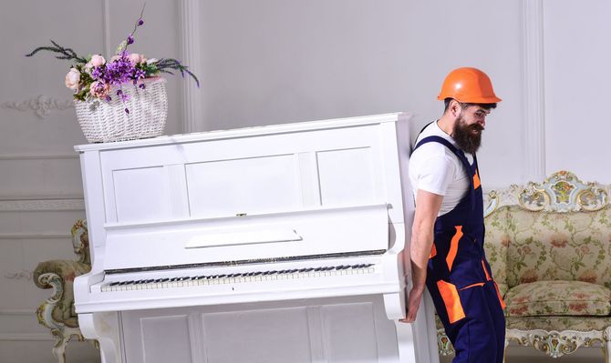 A man is carrying a white piano in a living room.