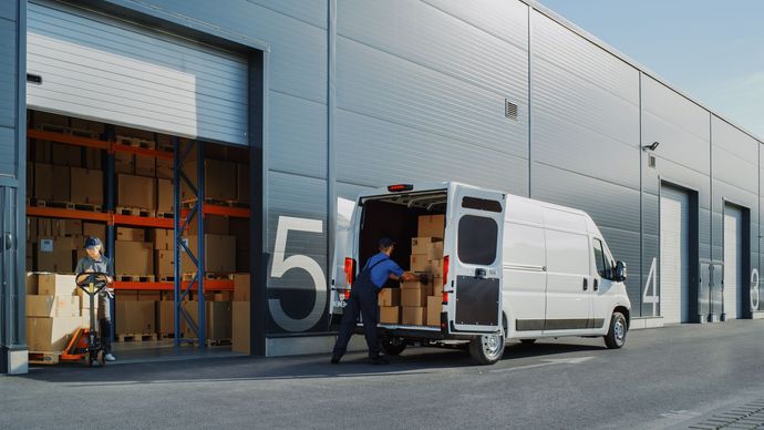 A man is loading boxes into a van in front of a warehouse.