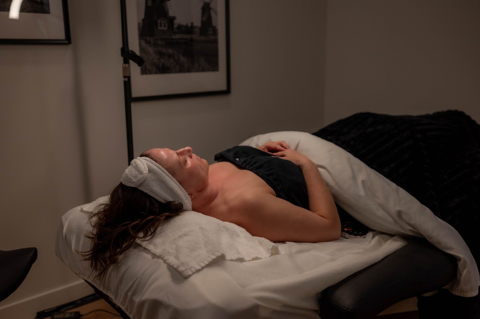 Person lying on a massage table with a towel over the eyes and a blanket draped over the body.