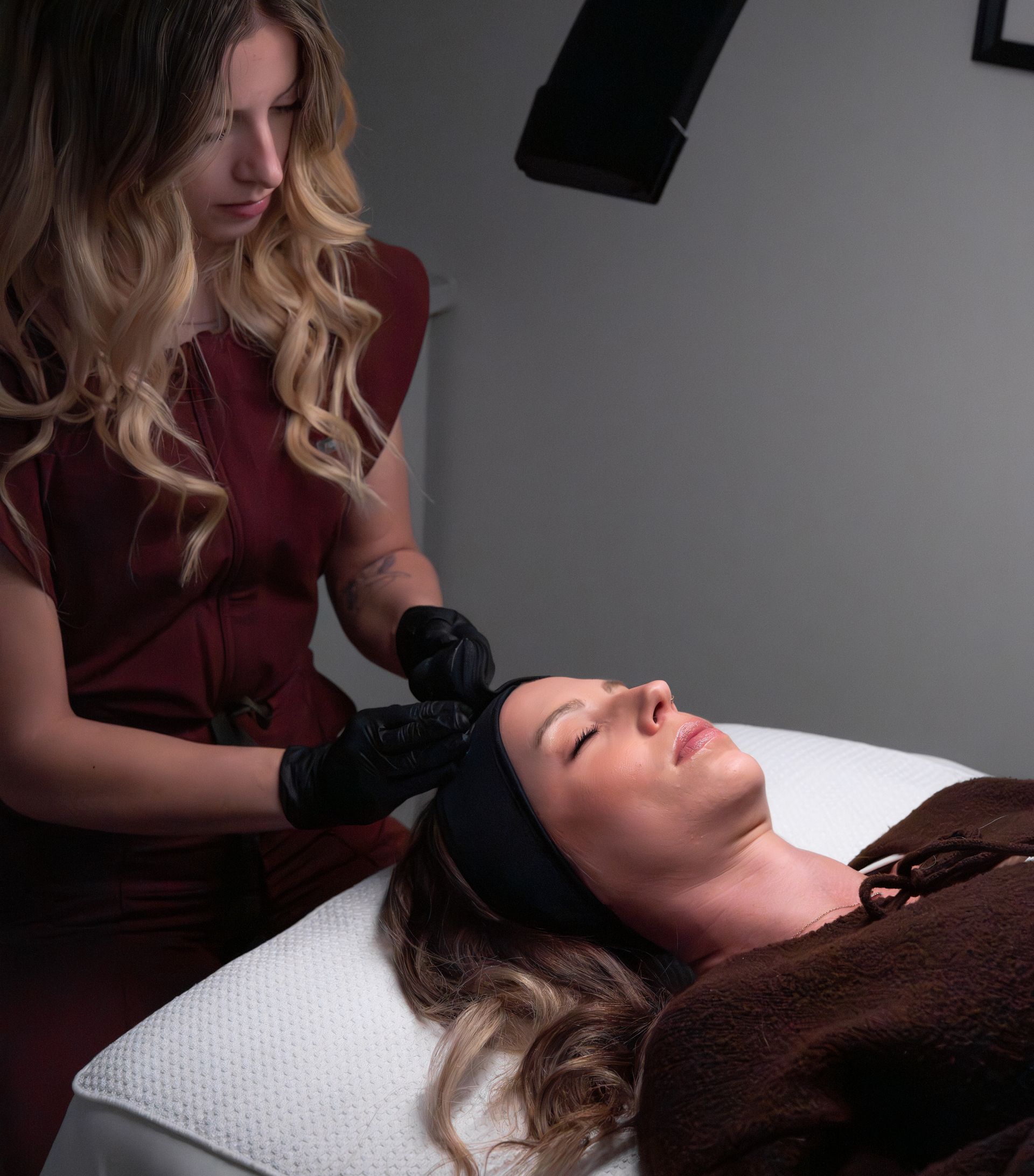 Esthetician applying treatment to a woman lying on a spa bed under a lamp