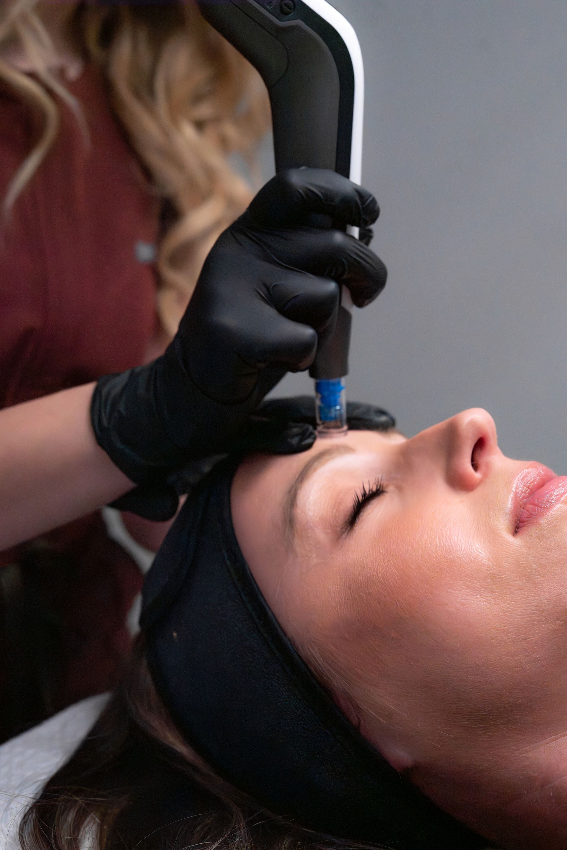 Esthetician using a handheld device on a client’s forehead during a facial treatment