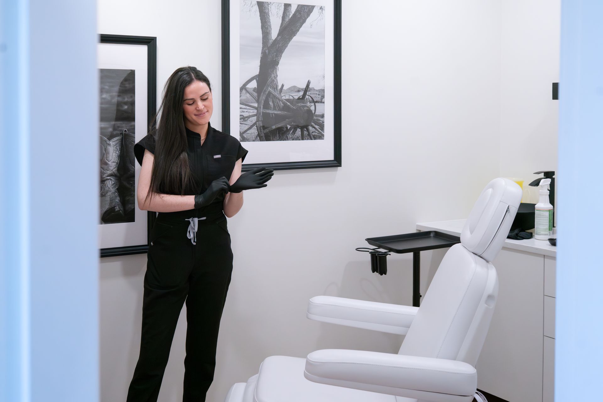 Woman standing in a modern clinic office beside a white treatment chair, holding a clipboard
