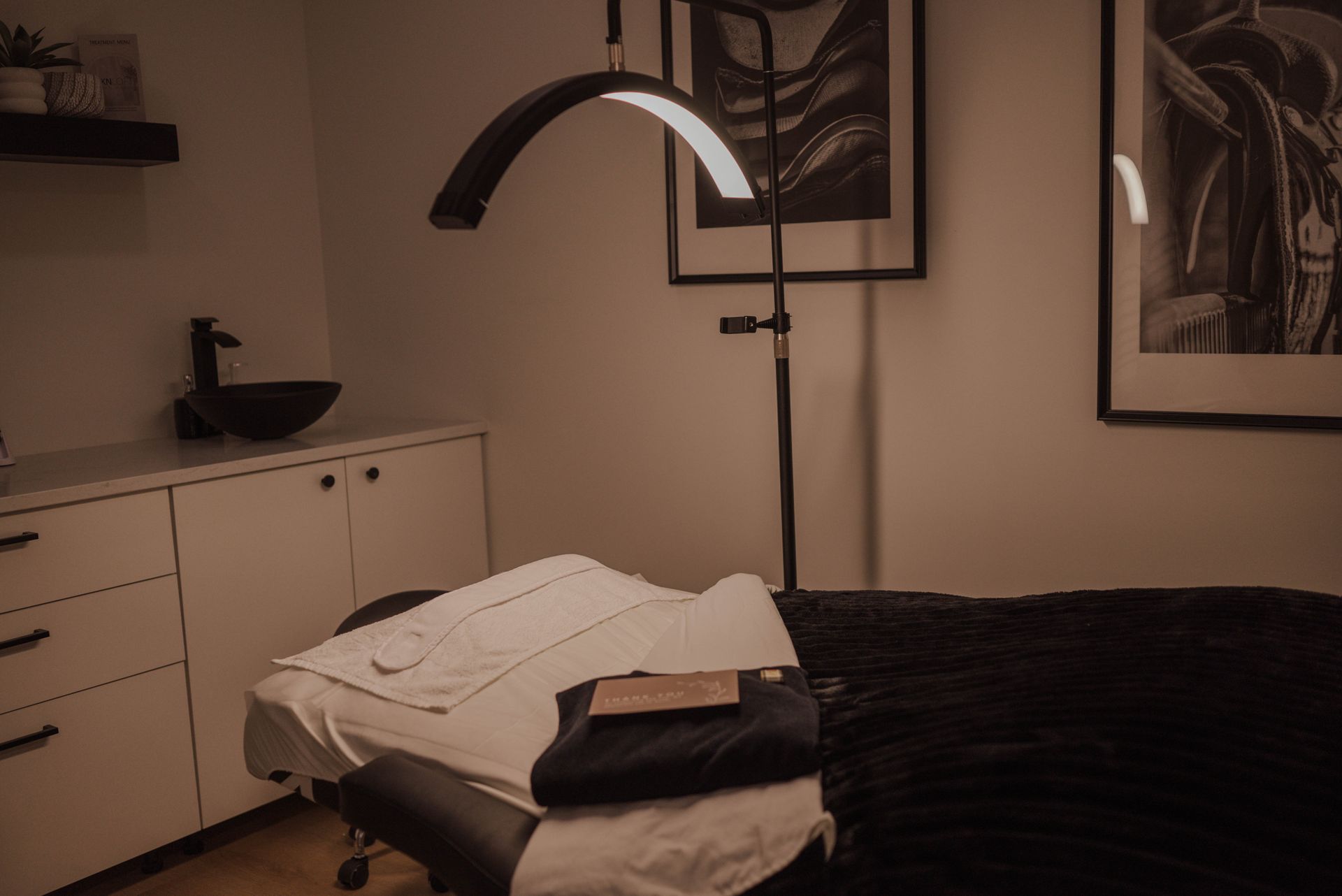 Massage room with treatment table, folded towel, lamp, and cabinets in soft lighting