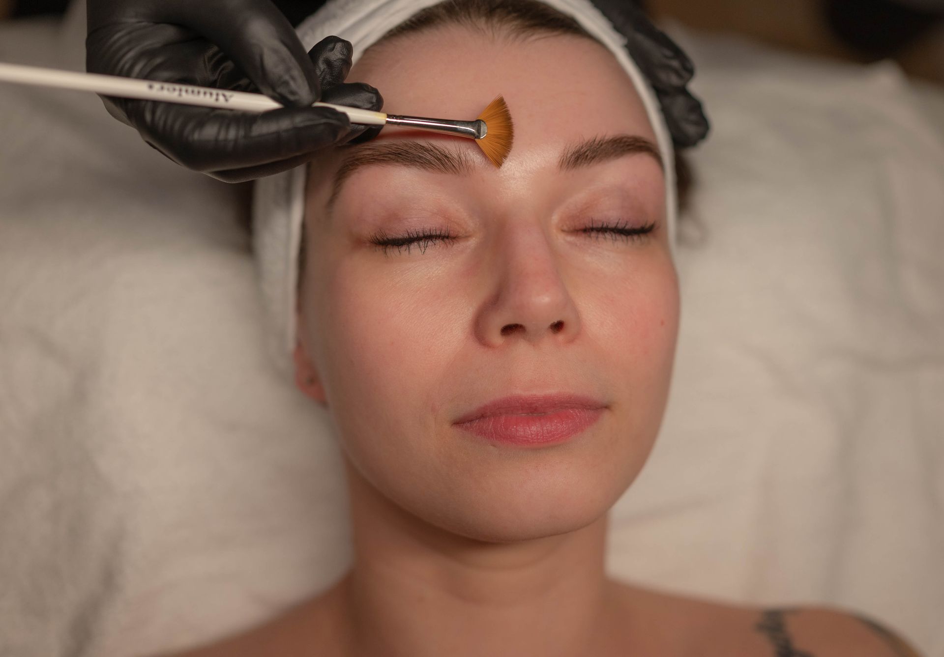 Spa facial treatment with a woman receiving serum applied to her forehead while lying on a treatment bed