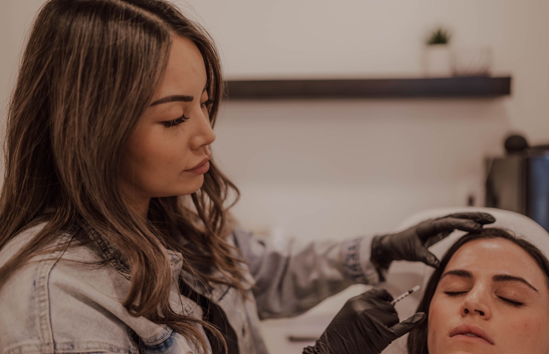 A cosmetologist applies treatment to a woman’s scalp in a salon spa setting.
