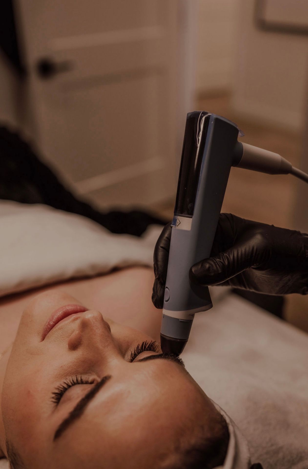 Cosmetic facial treatment with handheld device on a person’s forehead