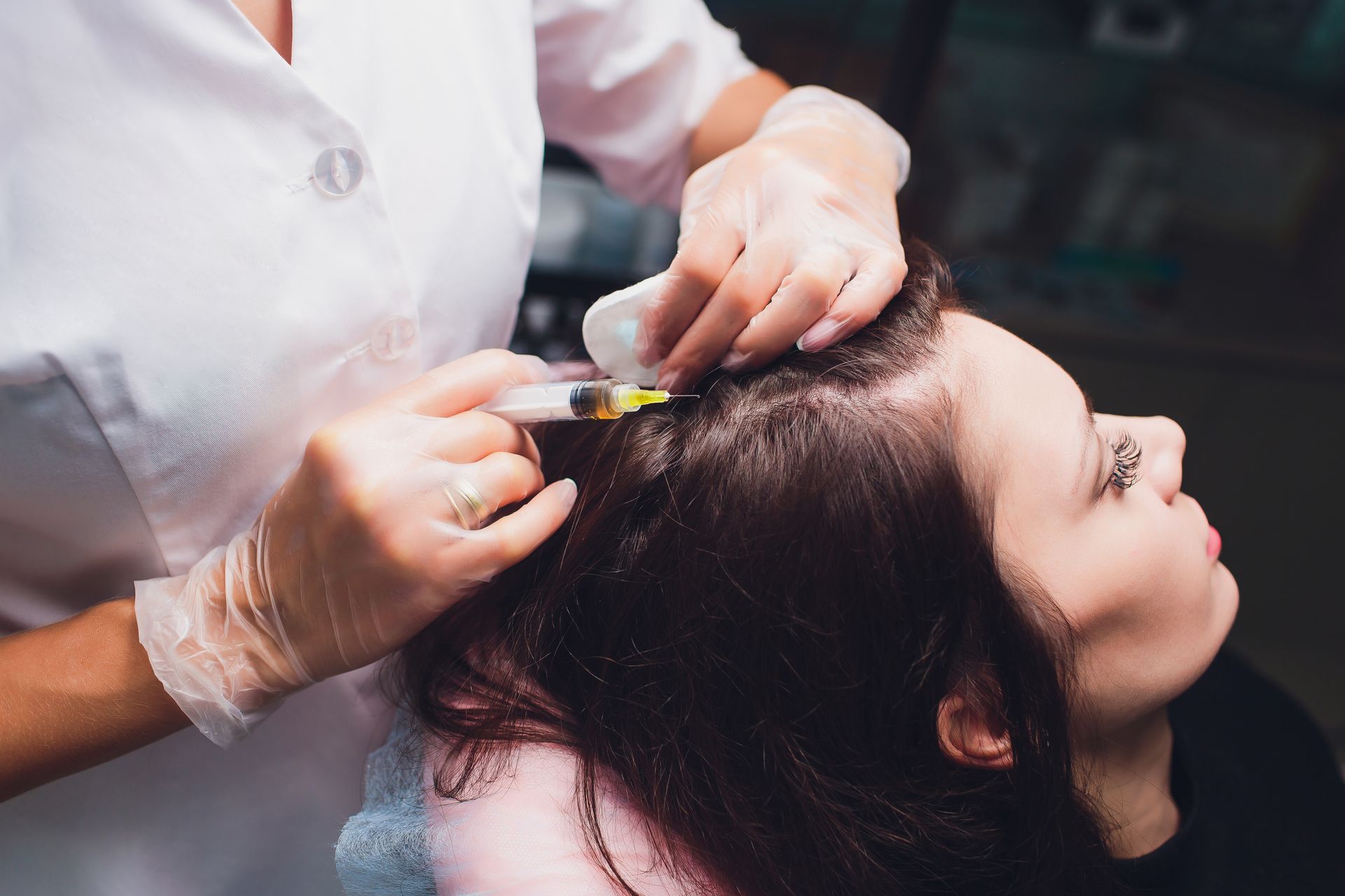 Gloved stylist applying treatment to a woman's hair at a salon sink