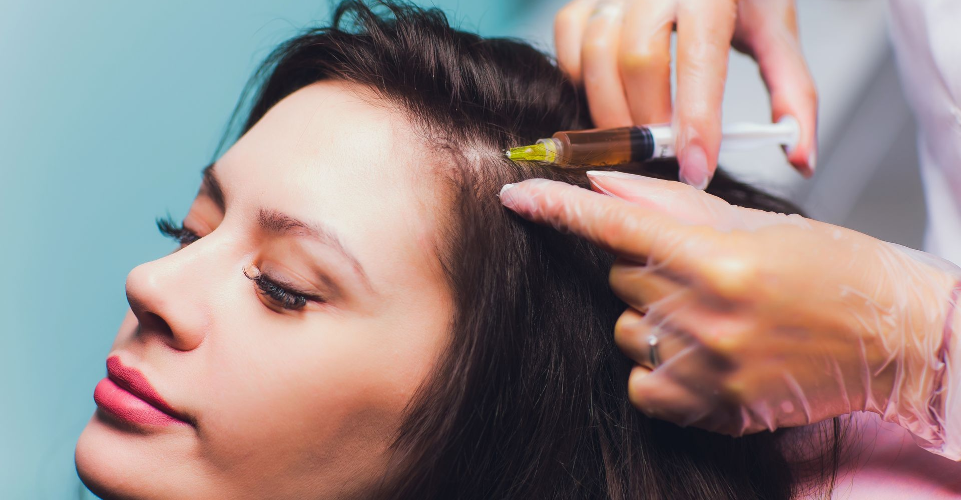 Stylist applying hair treatment with a brush to a woman’s dark hair while she reclines