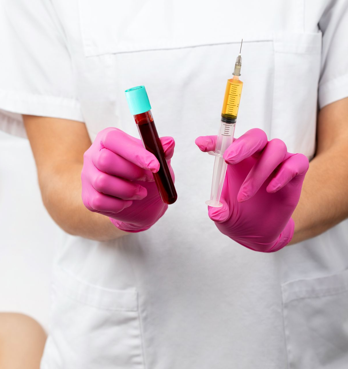 Gloved hands holding a blood sample tube and a syringe against a white medical coat