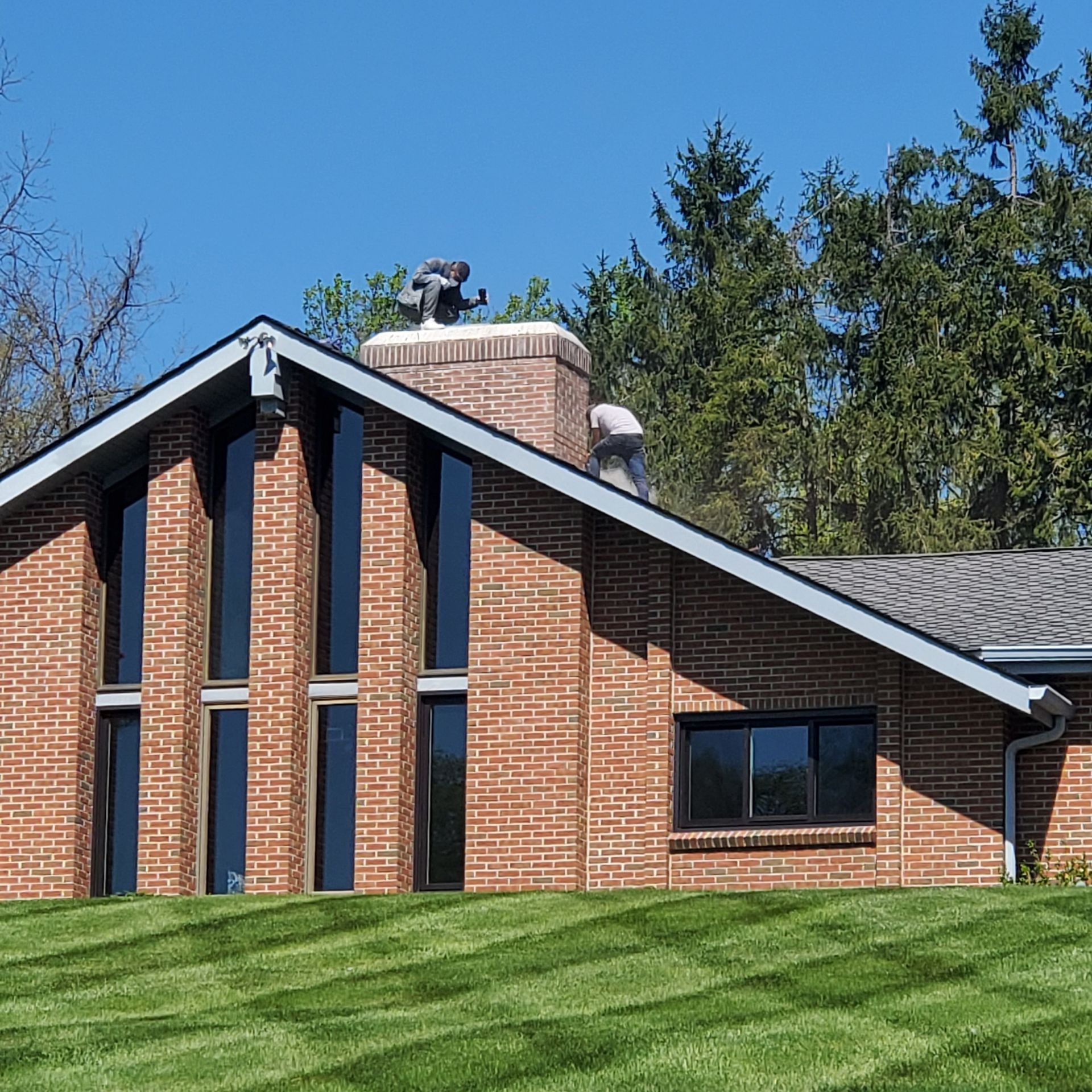Brick house with tall narrow windows and sloped roof on a grassy lawn under blue sky
