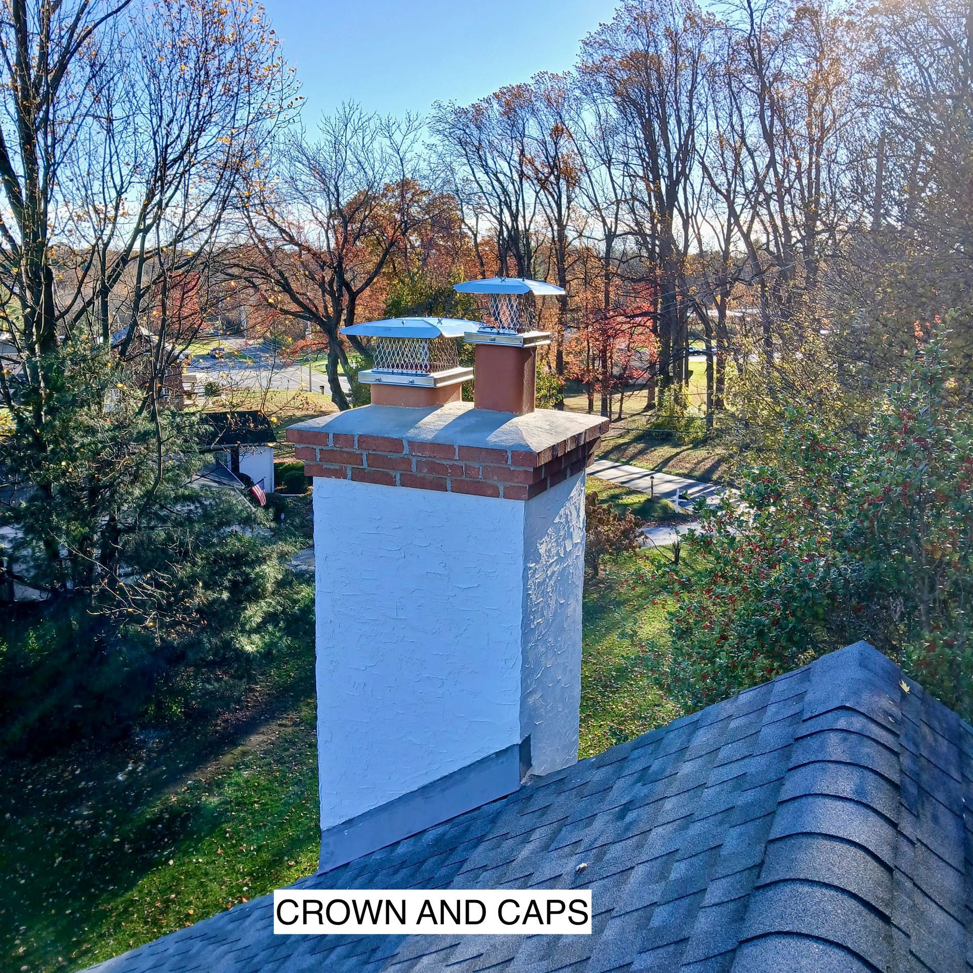A worker stands on a residential roof, inserting a flexible hose into a tall, gray chimney.