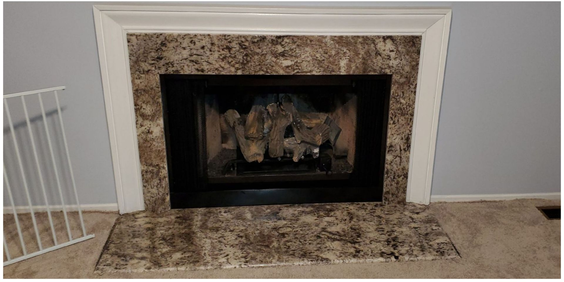 Stone fireplace with dark firebox and light mantel on a gray wall, with tiled hearth
