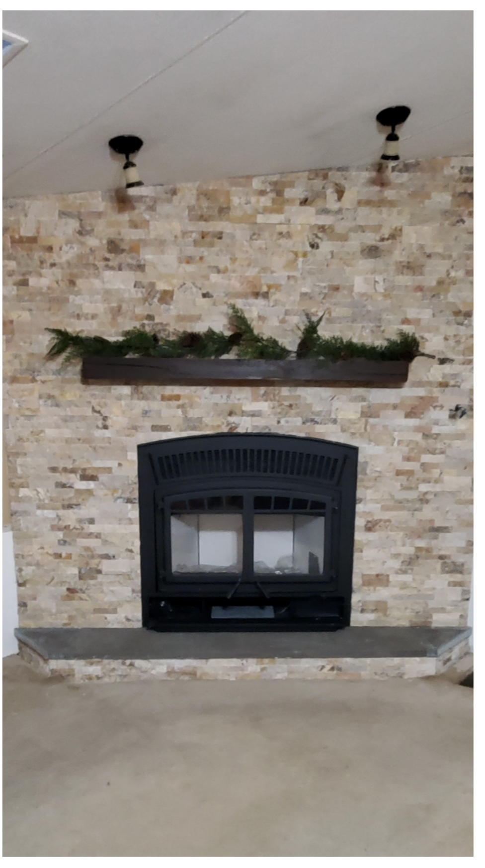 Stone fireplace with a black insert and shelf against a light brick wall.